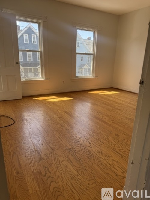A room with wooden flooring and two windows.