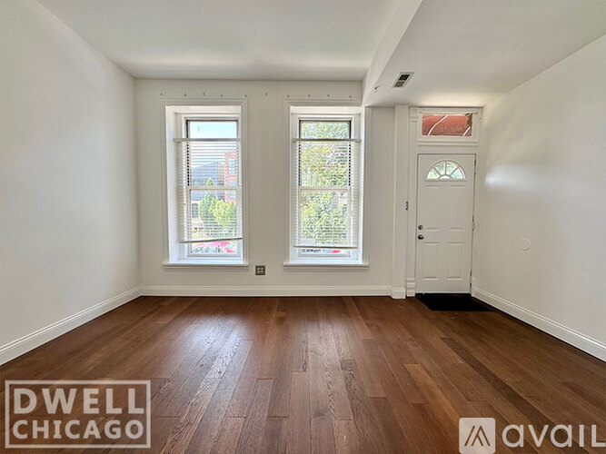 A room with wooden floors and white walls, with two windows and a door.