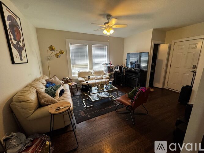A living room with a beige couch, a coffee table, a ceiling fan, and a television.