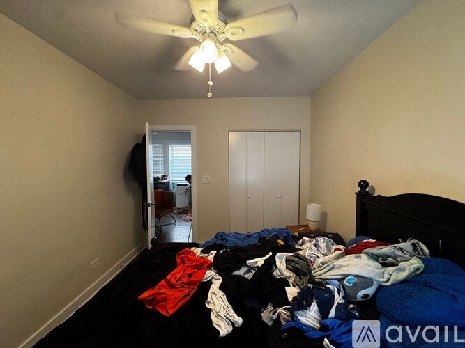 A bedroom with a bed covered in clothes and a ceiling fan.