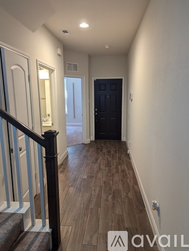 A hallway with a black door and wooden floors.