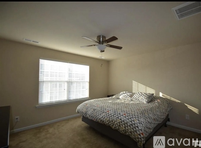 A bedroom with a bed, ceiling fan, and window with blinds.