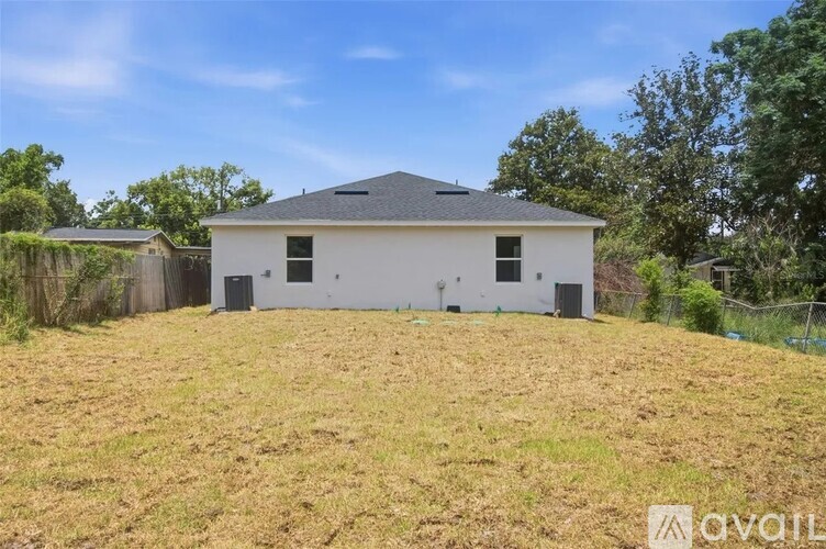 A white house with a black roof is situated in a grassy area with trees in the background.