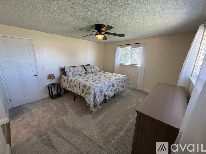 A bedroom with a bed, a fan, and a carpeted floor.