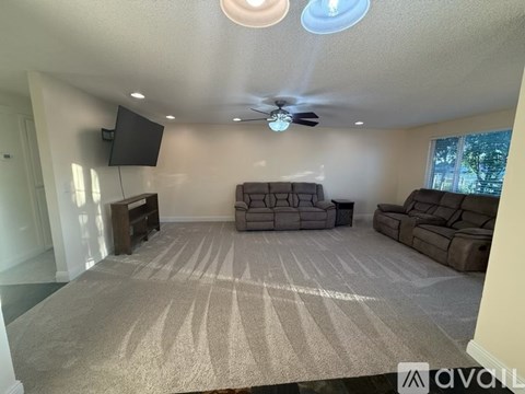 A living room with a carpet, a sofa set, a television and a ceiling fan.