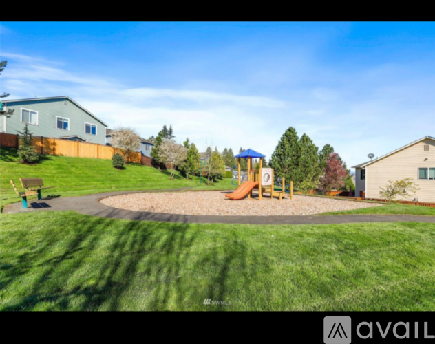 A playground with a slide and a round sandbox in the middle of a grassy area.