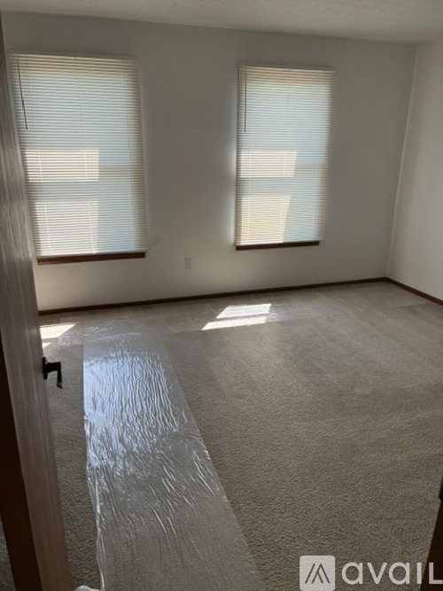 A room with a carpeted floor and two windows.