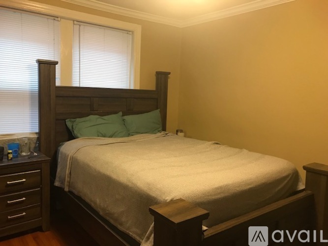 A bedroom with a bed, nightstand, and window with blinds.