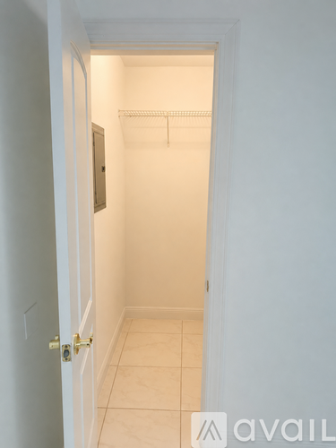 A white door with a gold handle is open to a small, empty room with white walls and tile flooring.