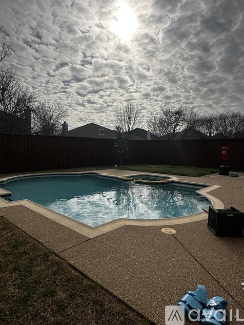 A pool surrounded by a concrete patio and a fence.