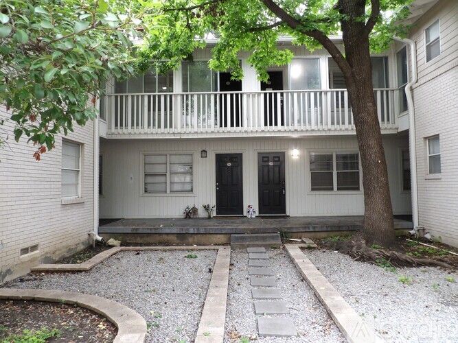 A white house with a black door and a tree in front.
