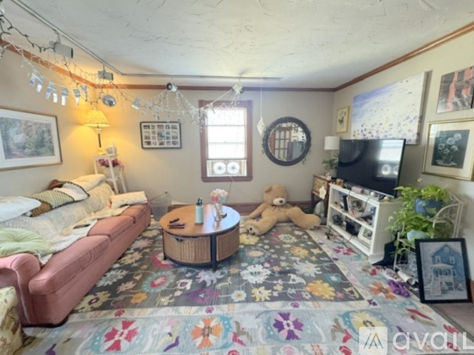 A cozy living room with a pink sofa, a coffee table, a teddy bear, and a TV.