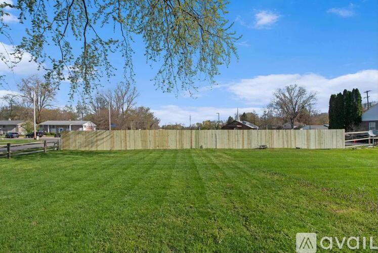 A grassy field with a wooden fence and trees in the background.