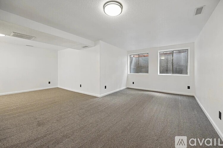 A spacious room with carpeted flooring and two windows with blinds.