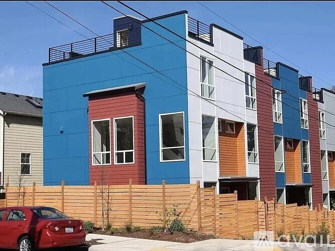 A red car is parked in front of a multi-colored building.