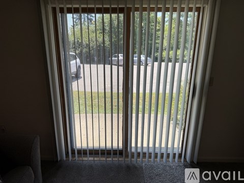 A view from a window with a white blind showing a parking lot and trees.