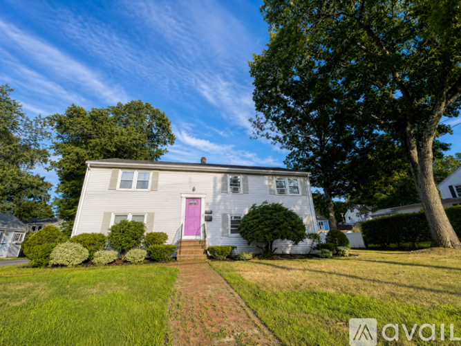 A house with a pink door is surrounded by greenery and a clear blue sky.