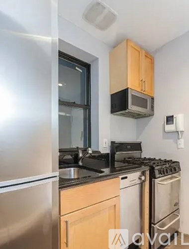 A kitchen with a stainless steel refrigerator, a microwave above the stove, and wooden cabinets.