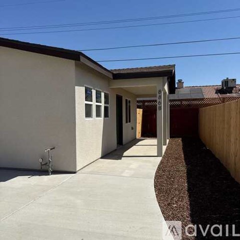 A house with a white exterior and a brown roof has a driveway in front.