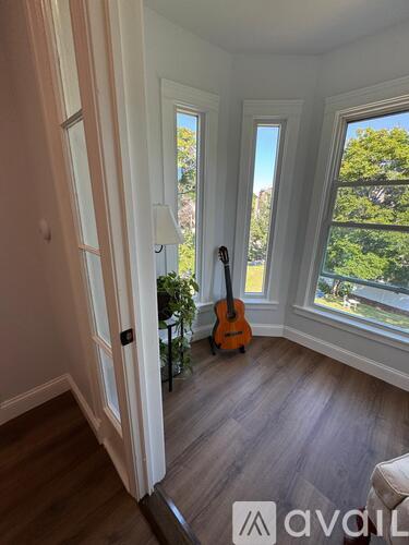 A room with a guitar leaning against the wall and a window showing trees outside.
