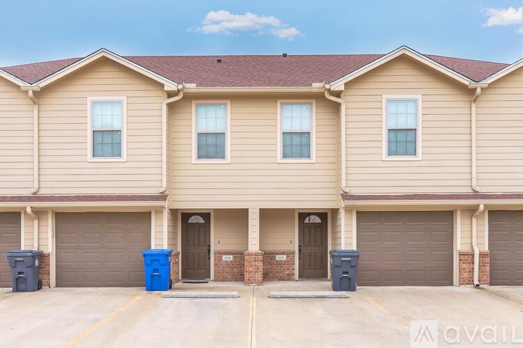 A row of houses with garages and blue bins in front.
