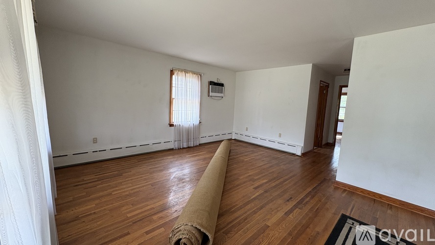 A room with wooden floors and white walls, with a roll of carpet on the floor.