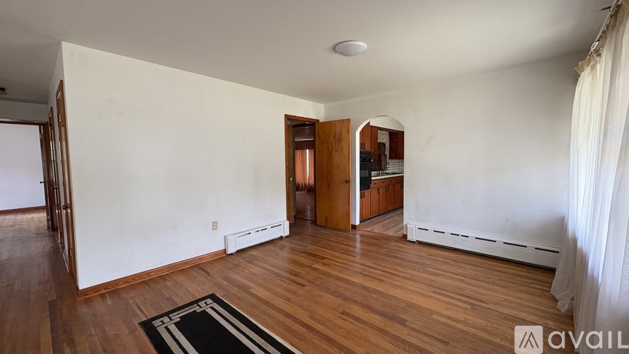 A room with wooden floors and a white wall with a doorway leading to another room.