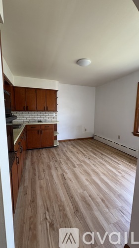 A room with wooden flooring and a kitchen area with cabinets and a stove.