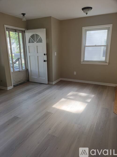 A room with a white door and a window with a wooden floor.