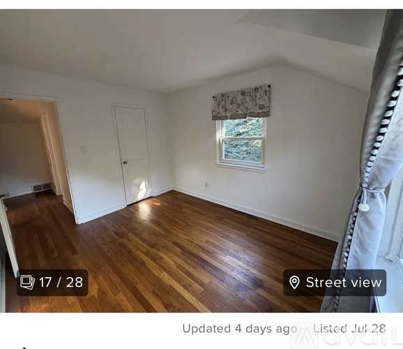 A room with wooden flooring and a window with a view of trees outside.