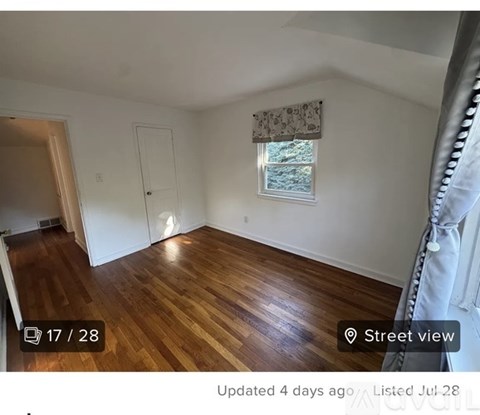 A room with wooden flooring and a window with a view of trees outside.