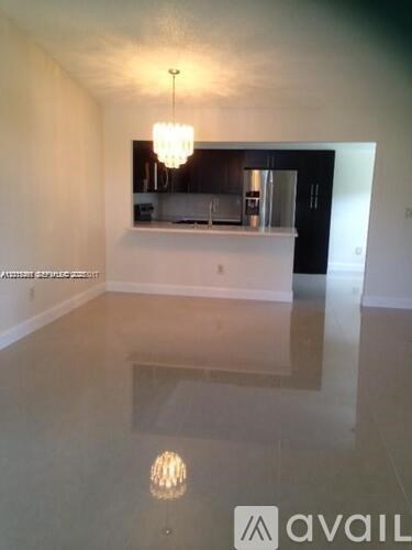 A large empty room with a chandelier and a kitchen in the background.