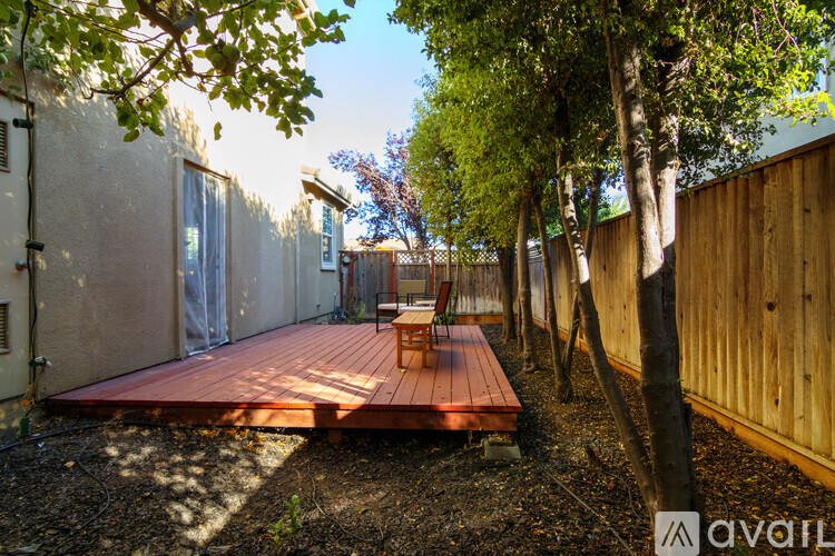 A wooden deck with a bench is surrounded by trees and a wooden fence.