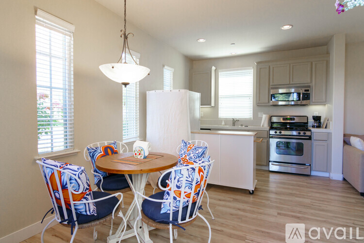 A kitchen with a table and chairs in the foreground and a refrigerator, oven, and microwave in the background.