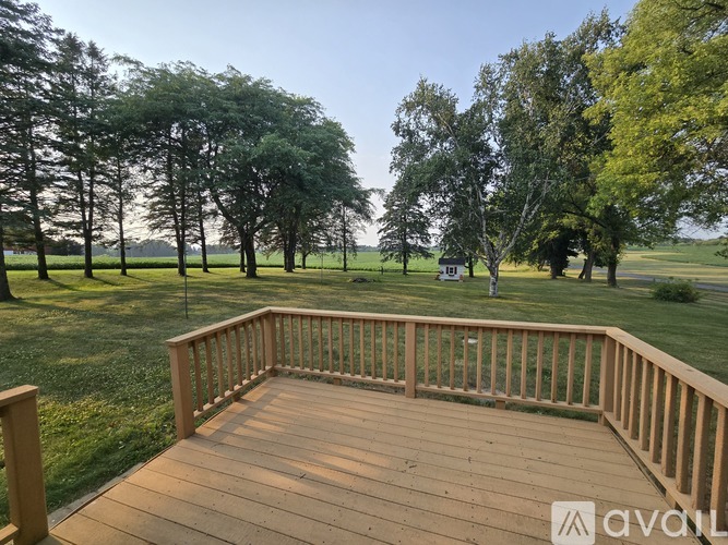 A wooden deck overlooks a grassy field with trees.