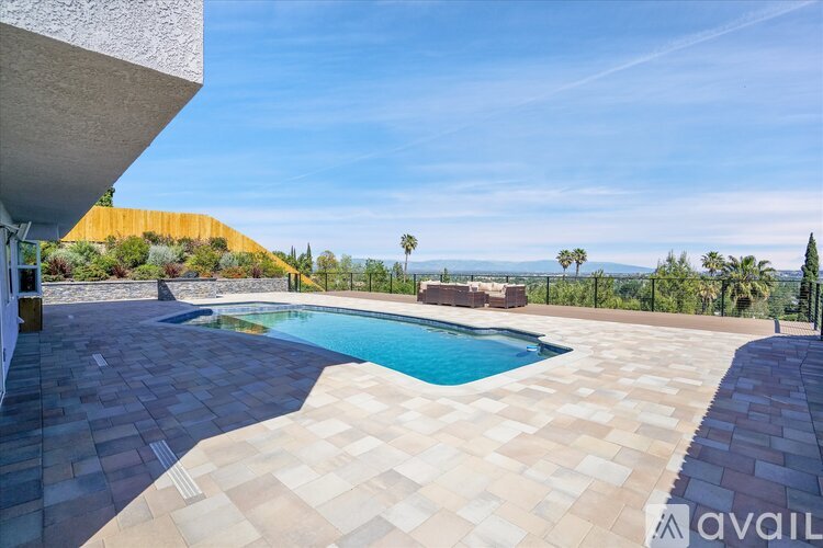 A pool surrounded by a tiled patio with a mountain view in the background.