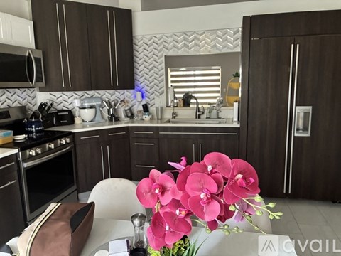 A kitchen with brown cabinets and a white countertop with a vase of pink flowers on it.