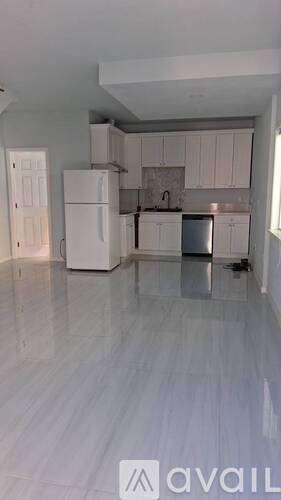 A kitchen with white cabinets and appliances in a large empty room.