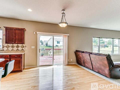 A living room with a brown couch and a kitchen area with brown cabinets.
