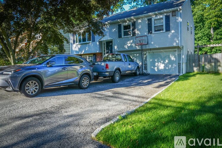 A silver car is parked in front of a house with a basketball hoop in the backyard.