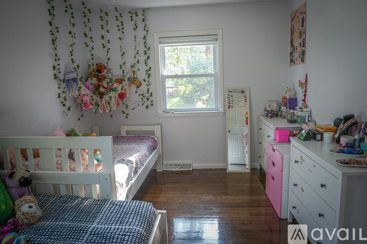 A child's bedroom with a white bed, a pink dresser, and a window with a view of trees.