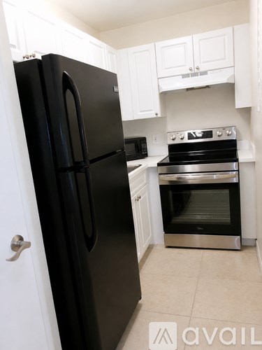 A black fridge in a kitchen with white cabinets.