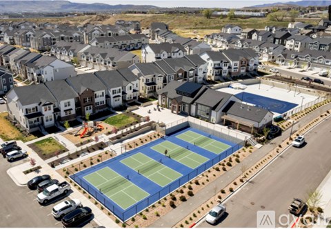 A tennis court is surrounded by a parking lot and residential buildings.