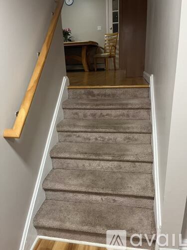 A staircase with a wooden handrail and carpeted steps leading to a dining area.