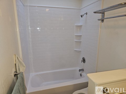 A white tiled bathroom with a bathtub and a towel rack.