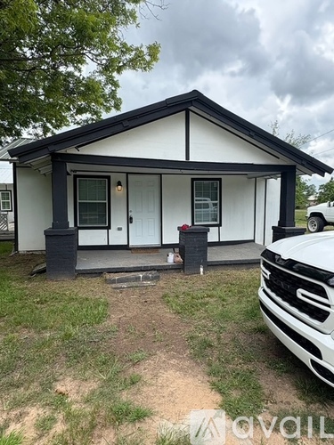 A small white house with a black roof and a black trash can in front of it.