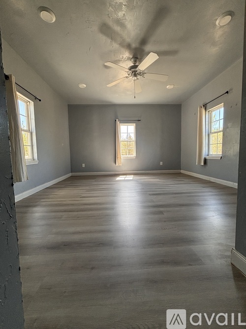 A spacious room with a ceiling fan and wooden flooring.