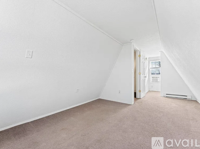 A room with white walls and carpeted floor with a doorway leading to another room.