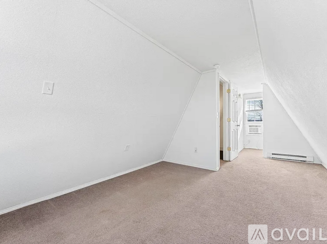 A room with white walls and carpeted floor with a doorway leading to another room.