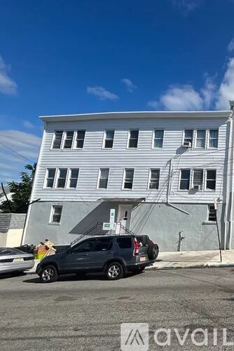 A white two-story building with a grey roof and a black car parked in front.